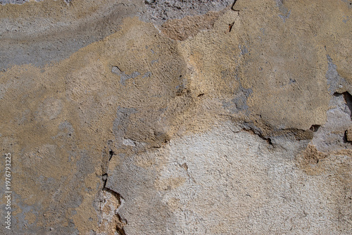 A close-up of an old beige plaster wall with peeling paint, cracked stucco an...