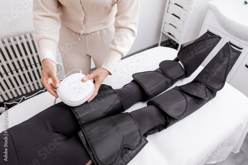 Therapist Operating Pressotherapy Machine While Female Client Lies with Full Leg Air Compression Boots on Massage Table — Professional Pneumatic Lymphatic Drainage Treatment for Legs, Anti-Cellulite 