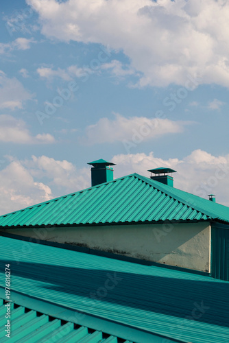 Bright teal metal roof with chimneys against blue sky
