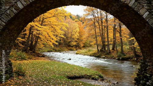 A picturesque view of a vibrant autumn forest and flowing river framed by a rustic stone archway.