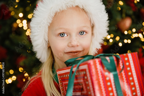 Merry Christmas and Happy Holidays. Little child under Christmas tree. baby girl in Santa Claus hat with gifts under Christmas tree with many gift boxes presents. Happy Holidays, New year.