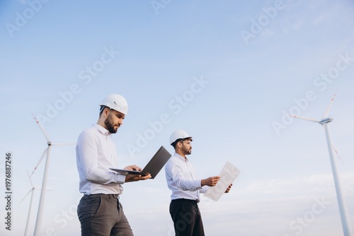 Engineers working on a wind turbine project using laptop and blueprints