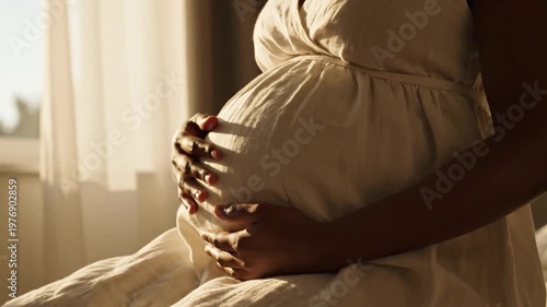Close-up of a pregnant woman gently cradling her belly in soft, warm morning sunlight