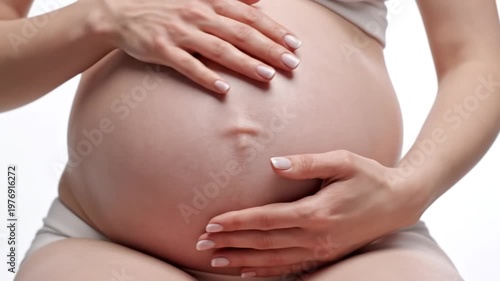 Close-up of a pregnant woman gently caressing her bare belly with hands on white background