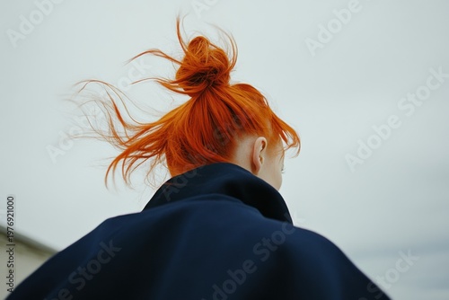 Minimalistic portrait of woman with vibrant red hair in wind against clear sky