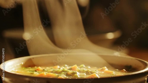 A steaming bowl of fresh vegetable soup with visible carrots and peas in a warm kitchen setting