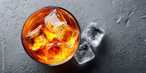 Amber whiskey with ice cubes in a glass on a textured grey surface