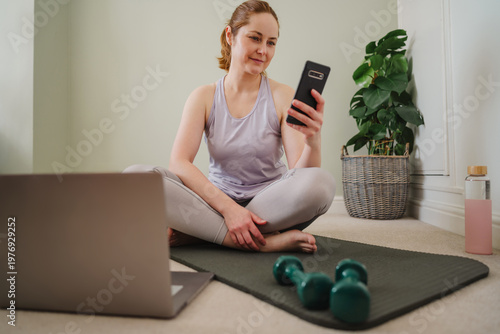 Woman following online fitness workout on mat with dumbbells at home