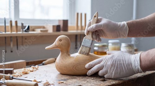 Wooden duck figurine being painted by a male artisan wearing gloves in a workshop with various tools and materials visible in the background