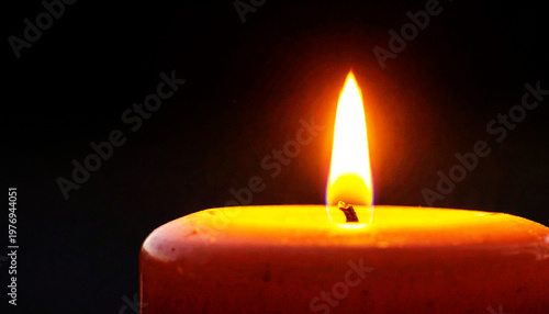 Single candle flame glowing in the dark with warm orange light
