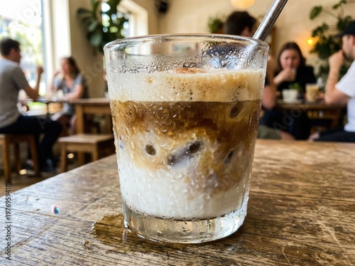 Close-up shot of iced coffee drink on wooden table in cafe with people