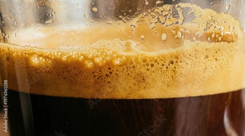 A close-up shot of a glass filled with dark beer and a layer of foam on top.