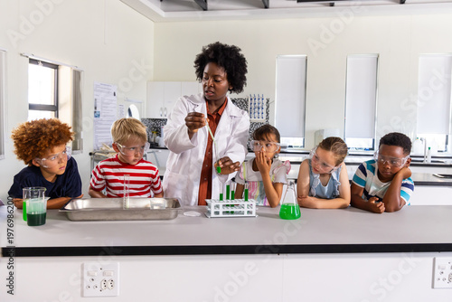 African American teacher guiding kids with goggles using pipette mixing green liquid at lab bench
