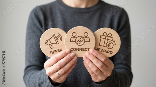 Person holding three wooden circles with refer, connect, and reward icons, illustrating a referral program concept.