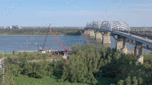 Aerial view of a long train crossing a bridge alongside vehicular traffic, showcasing an industrial landscape, New Orleans, Louisiana, United States.
