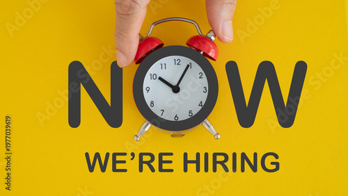NOW we are hiring text on grunge yellow background with analog alarm clock instead of O alphabet