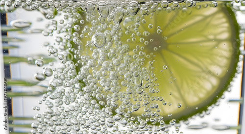 Tiny bubbles rise in a glass of sparkling water with lime.