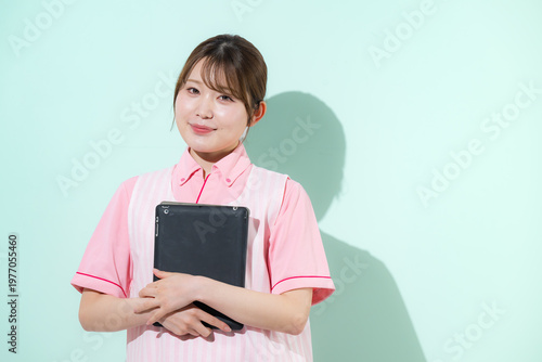 グリーン背景で介護士や保育士として働く女性の訪問介護とやりがいある仕事のイメージ　転職などのイメージにカメラ目線の笑顔　タブレットを持つ