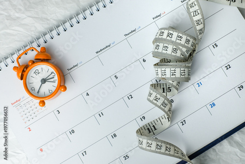 Tableau sur toile Orange alarm clock placed on a calendar page with a measuring tape arranged along the side