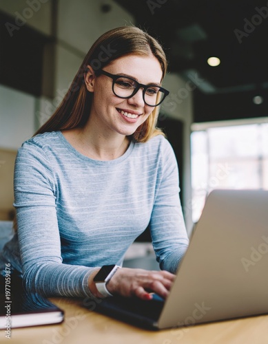 Young smiling woman wearing glasses using laptop at a modern cafe, enjoying remote work and online learning experience