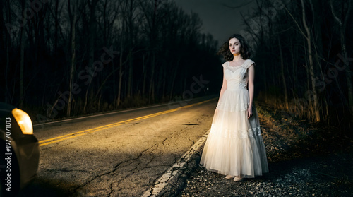 Woman in white dress standing alone on dark road at night