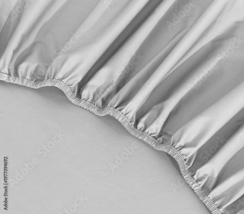 White fitted sheet against a white background. Fitted sheet or bed cover crumple. White sheet with elastic band bed corner, Bed skirt closeup photo