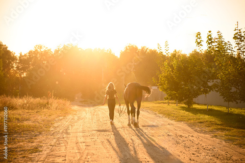 Foto Woman leading horse down dirt road at sunset, back view of friendship and trust