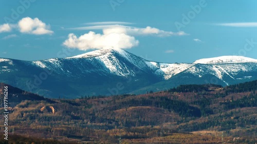 Zoom on Snezka mountain peak in Sudetes on Czech-Polish border, April, clouds, blue sky.
