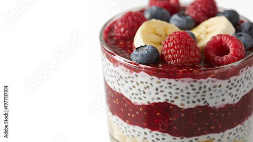 Layered raspberry chia seed pudding with banana slices and blueberries in a glass on white base