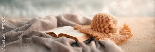 Straw hat and open book on soft blanket on sandy beach with blurry ocean background, perfect for relaxing summer vacation