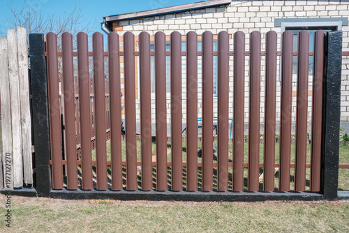 Modern brown metal euro fence panels home garden w section palisade picket with vertical slats and black posts. New privacy fencing, showcasing property boundary and residential security.