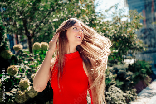 Fotografie Happy woman in a red dress with long hair enjoying sunlight outdoors in an urban