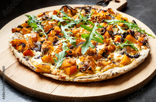 Homemade Hokkaido pumpkin pizza with arugula and balsamic glaze on wooden board