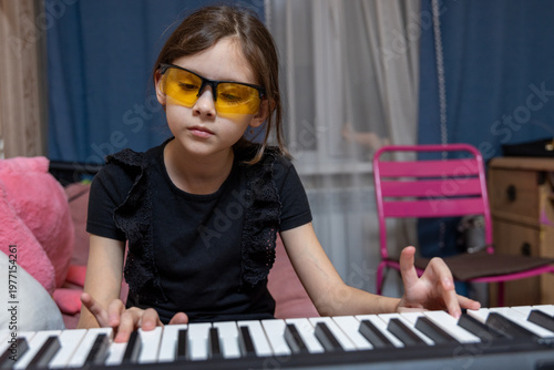 Portrait of a focused young girl wearing yellow protective glasses playing a digital piano at home.