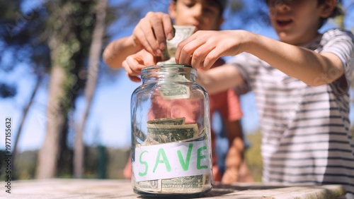 Quadro su tela Children learning about saving money, putting dollar bills into a transparent gl