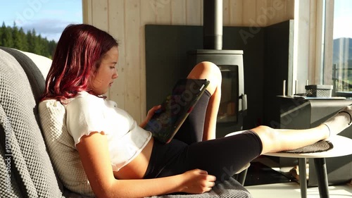 Girl sitting on couch looking at tablet while resting leg on table in modern living room