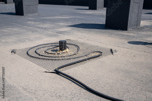 Heating cable installation with wire mesh around a roof drain on a flat bitumen surface for winter de-icing.