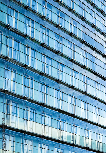 Blue glass facade of a modern building reflecting light and sky, showcasing contemporary architecture and clean geometric lines