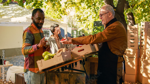 Foto Senior farmer and young vendor talking to diverse couple at local street fair, selling fresh homegrown products outdoors