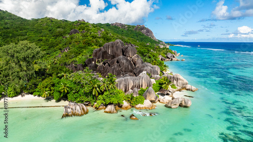 Granite rocks meeting turquoise water on a tropical coastline with lush greenery. Anse Source d'Argent. Seychelles, La Digue.