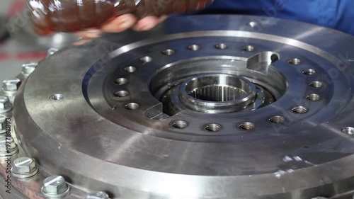 Mechanic pouring oil from a bottle to lubricate a bearing inside a heavy duty transmission housing during maintenance in a workshop.