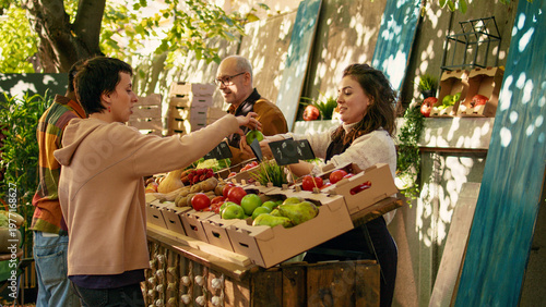 Young vendor giving free apple samples to clients, having fun with fresh products sampling at local greenmarket. Woman cutting slices of fruits to give to customers, small business owner.