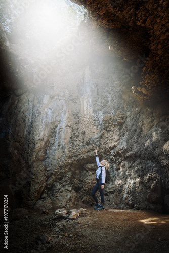 Hiker looking at a sunbeam inside a coastal cave in Italy.