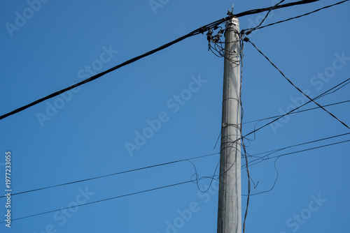 Fotografi Concrete utility pole with messy power lines against blue sky