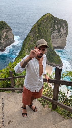 Man exploring Kelingking Beach in Bali Indonesia, tropical paradise with ocean cliffs and panoramic viewpoint, traveler descending iconic trail, happy raised pose enjoying adventure journey on exotic 