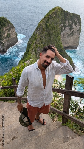 Man exploring Kelingking Beach in Bali Indonesia, tropical paradise with ocean cliffs and panoramic viewpoint, traveler descending iconic trail, happy raised pose enjoying adventure journey on exotic 