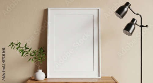 Elegant vertical white photo frame mockup leaning on a wooden console against a warm beige wall with a small plant in a white vase and a black lamp product mockup design