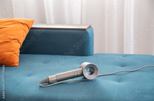 A dark gray hair dryer lies on a blue sofa in the living room, an electrical appliance for personal hygiene, an affordable household item