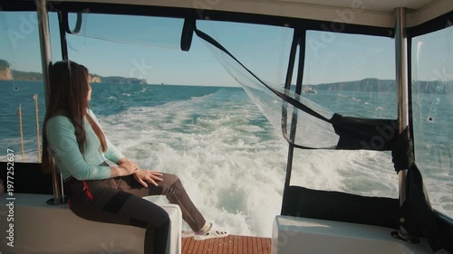 Young beautiful woman sits on stern of yacht and admiring views of bay with mountain ranges on coast. Slow motion. Concept of freedom and privacy