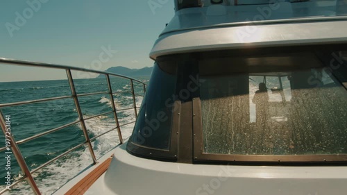 Yacht moves at high speed through sea bay leaving seething wake on water and silhouette of couple in cabin through glass. Travel and tourism concept